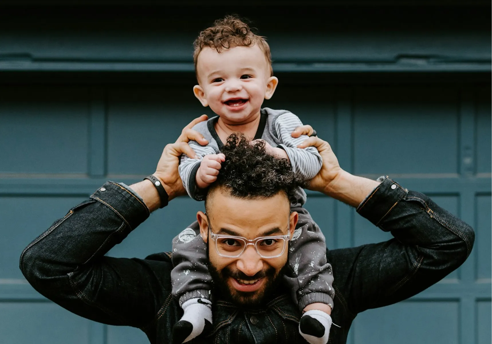 A father laughing with his young child on his shoulders